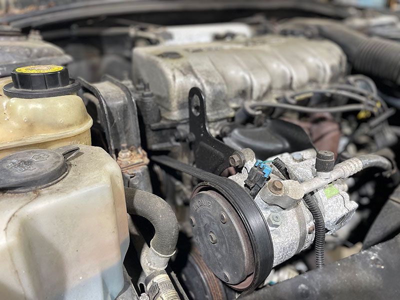 Car engine with a black belt, hoses, and various components visible.