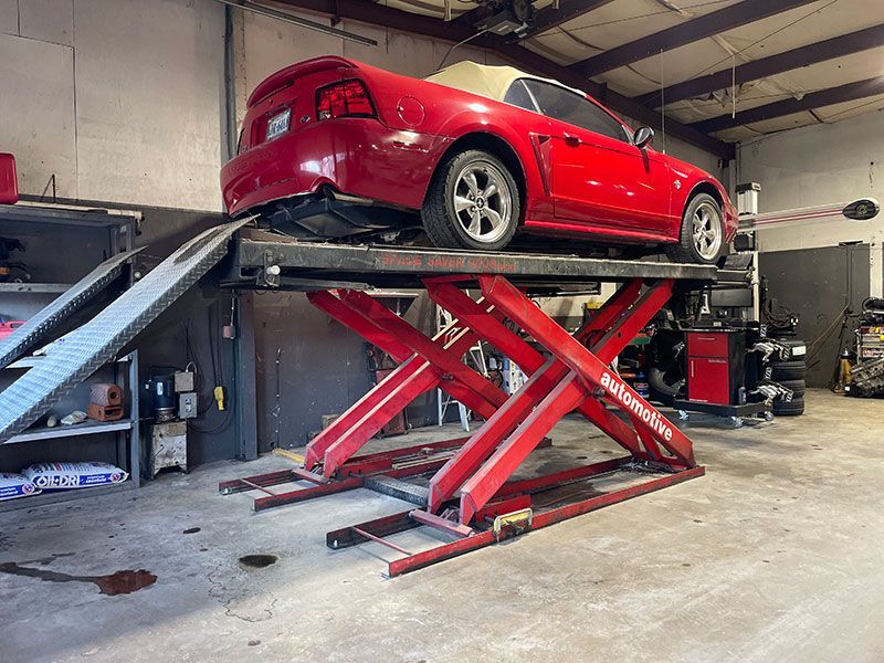 Red convertible on a red scissor lift in a garage.