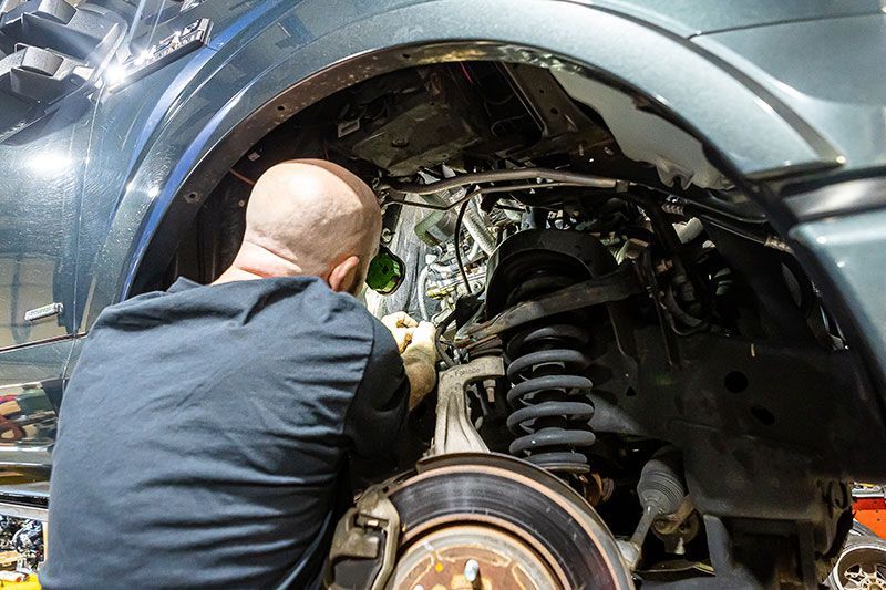 Mechanic working on the front wheel suspension of a vehicle. Dark colors, indoor setting.