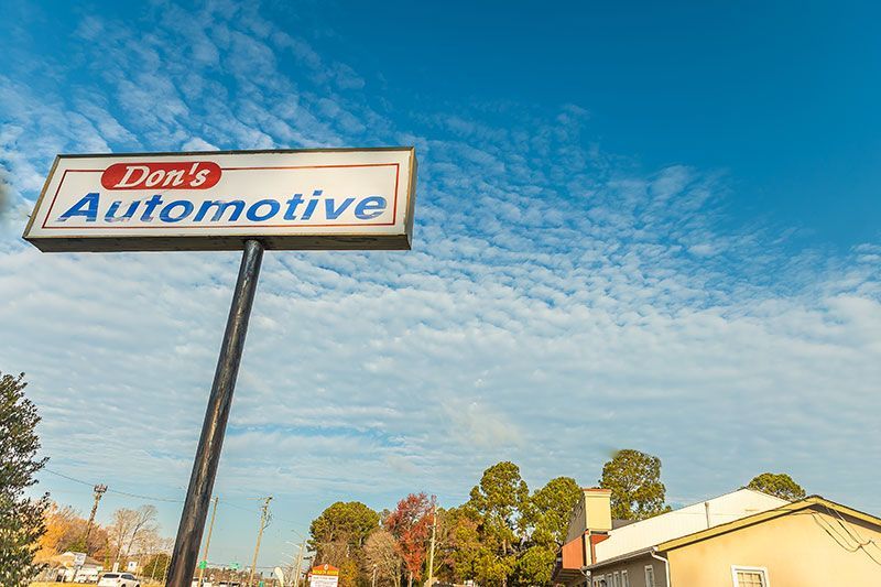 Sign for Don's Automotive against a blue sky with clouds, trees and a building in the background.