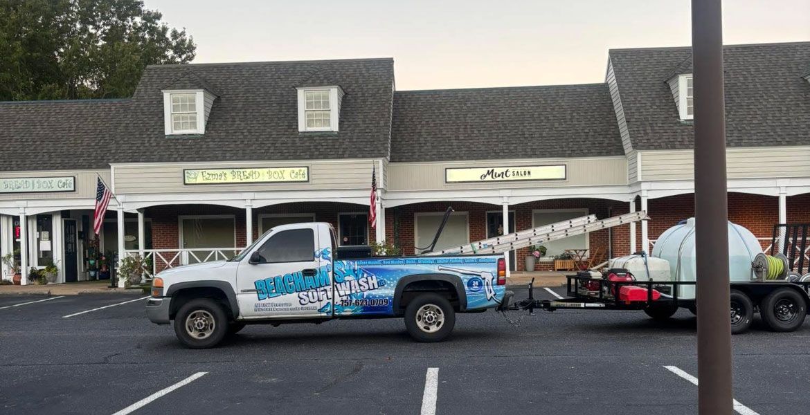 White pickup truck with trailer parked in front of a shopping center. The truck has blue graphics.
