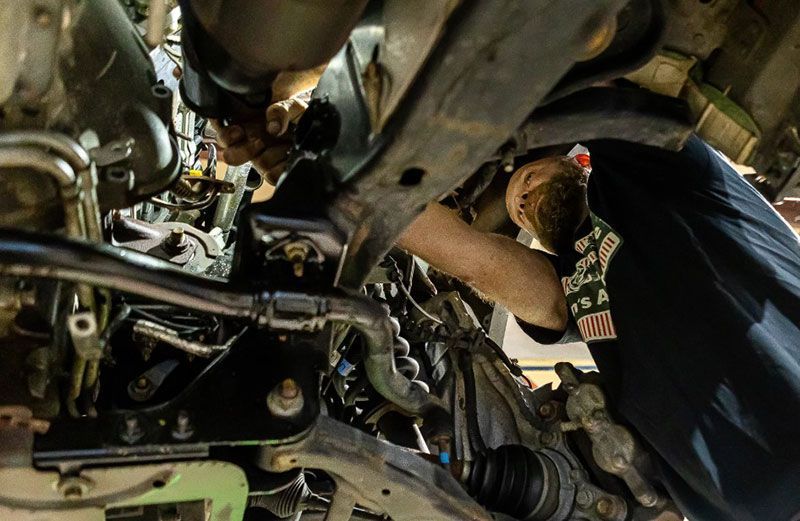 Two people working on the underside of a vehicle.