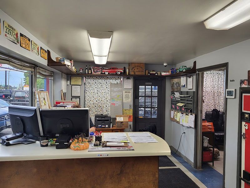 Interior of a car repair shop's front desk.  A curved counter with computer monitors and papers, cluttered with various items.