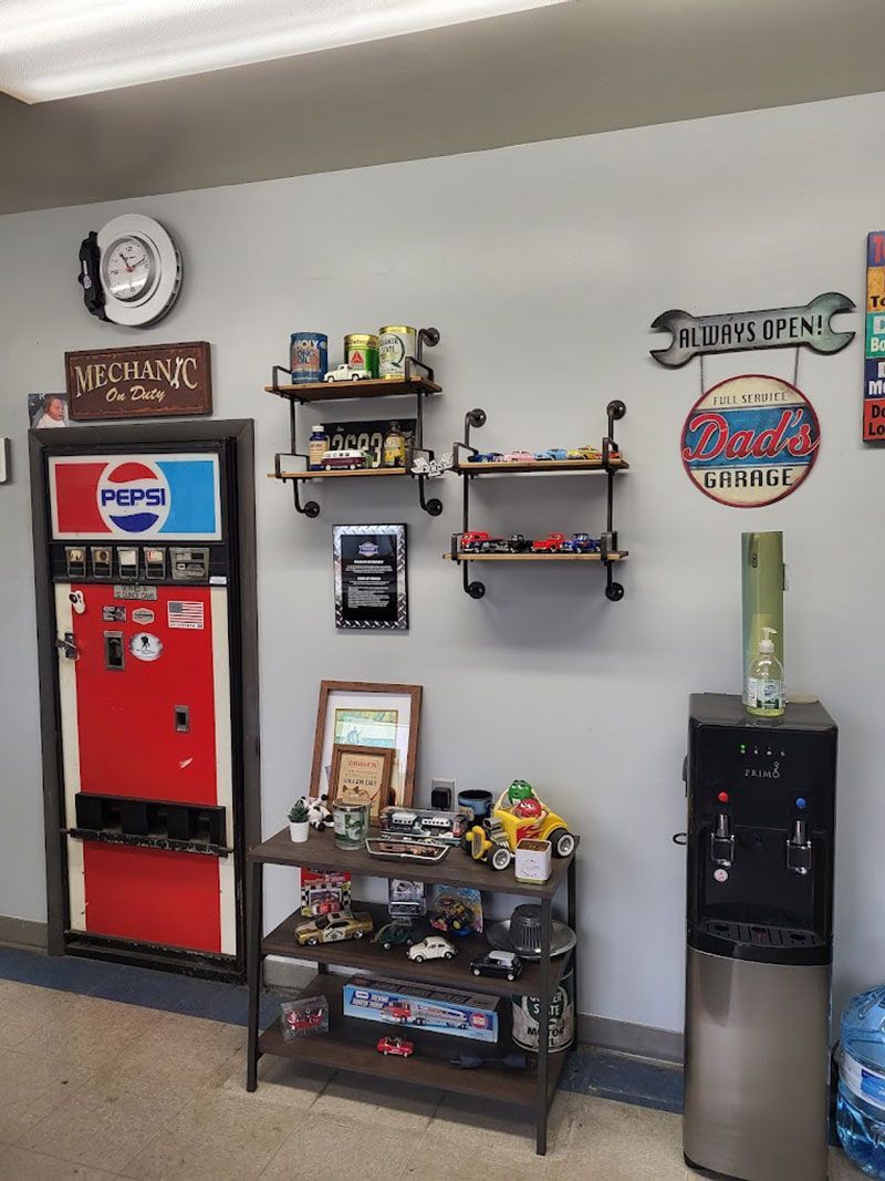 A shop interior with a Pepsi machine, shelves displaying items, and a water cooler against a gray wall.