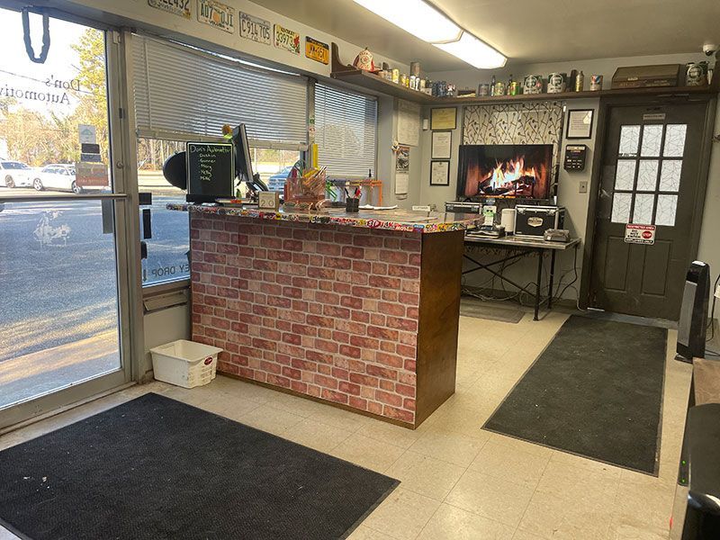 Interior of an auto repair shop with a reception desk, brick-patterned front, and a television playing a fireplace scene.