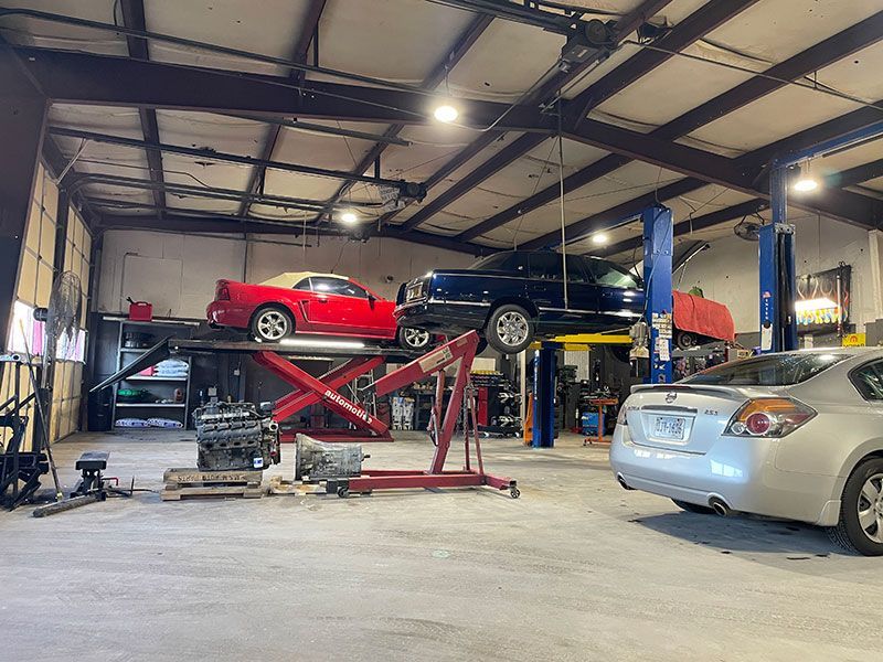 Auto repair shop with cars on lifts, tools, and a car engine on the floor.