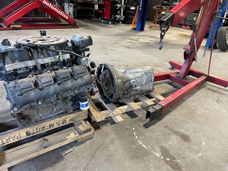 Engine and transmission on a pallet in a repair shop, near a red hoist.