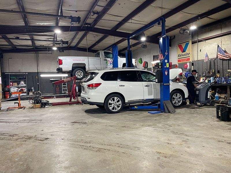 An auto repair shop with vehicles on lifts. A white SUV is being worked on by a person.