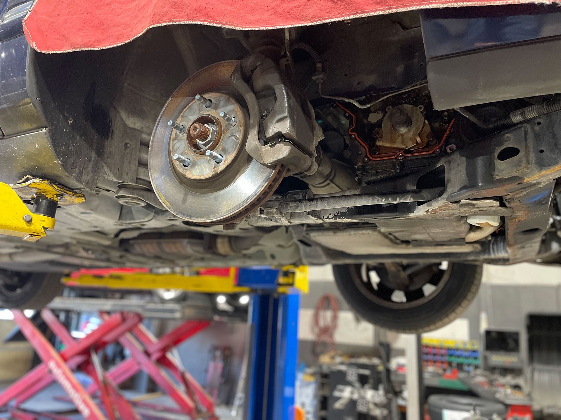 Car lifted on a hoist, revealing brake rotor, caliper, suspension components, and undercarriage.