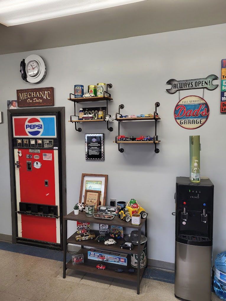 Interior of an auto shop with a vintage Pepsi machine, shelves of collectibles, and a water cooler.