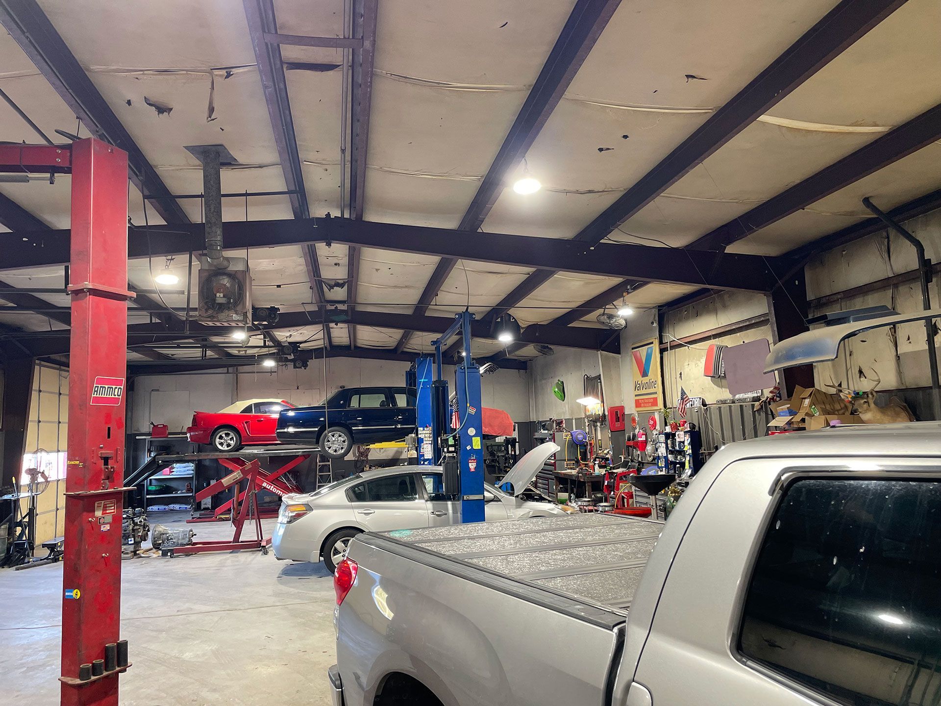 Inside auto repair shop; cars on lifts, mechanics working. Silver truck in foreground.