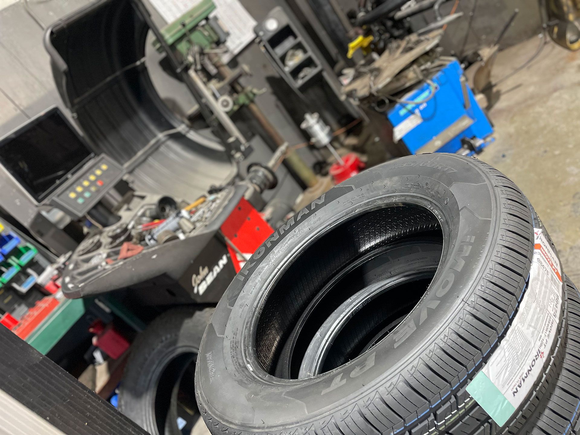 Tires stacked in a tire shop, with a wheel balancing machine in the background.