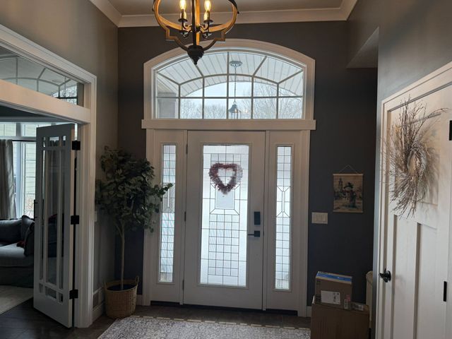 Front entryway with white double doors, transom windows, and a heart wreath in a dim hallway.
