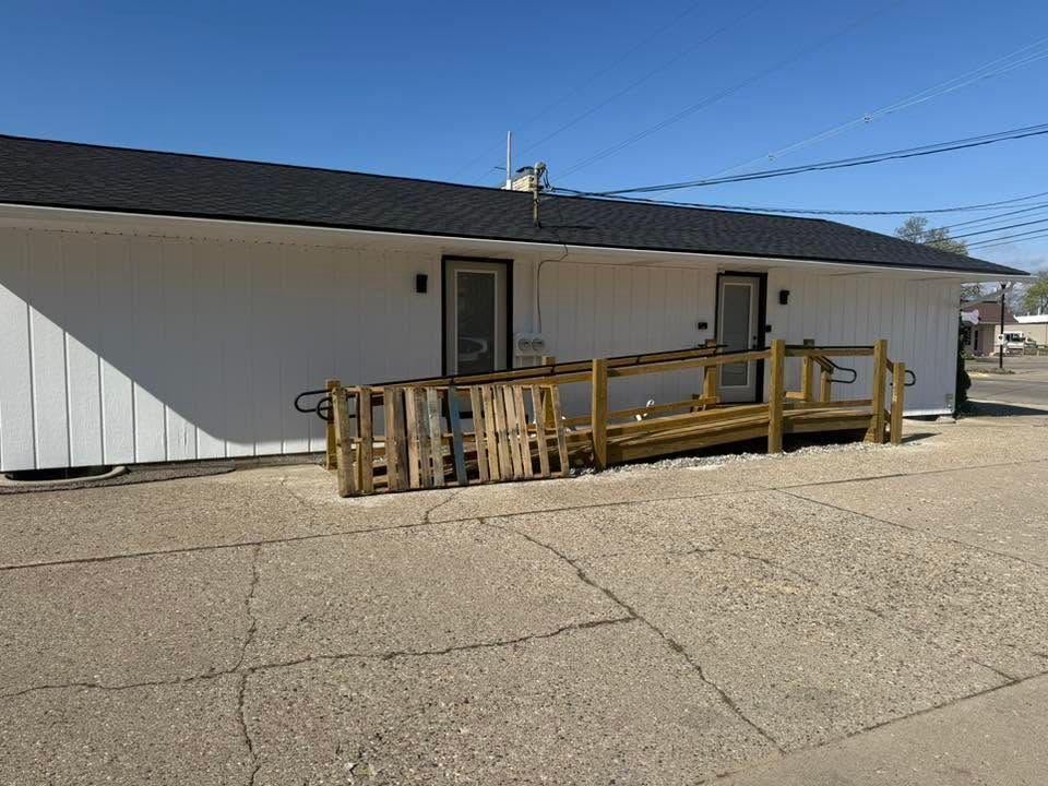 White building with a wooden handicap ramp and railing in a paved parking lot under a blue sky