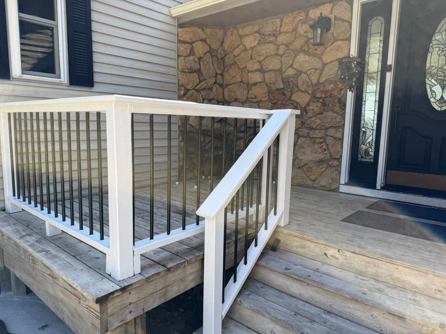 Front porch entrance with white railing, stone wall, and black front door beside steps