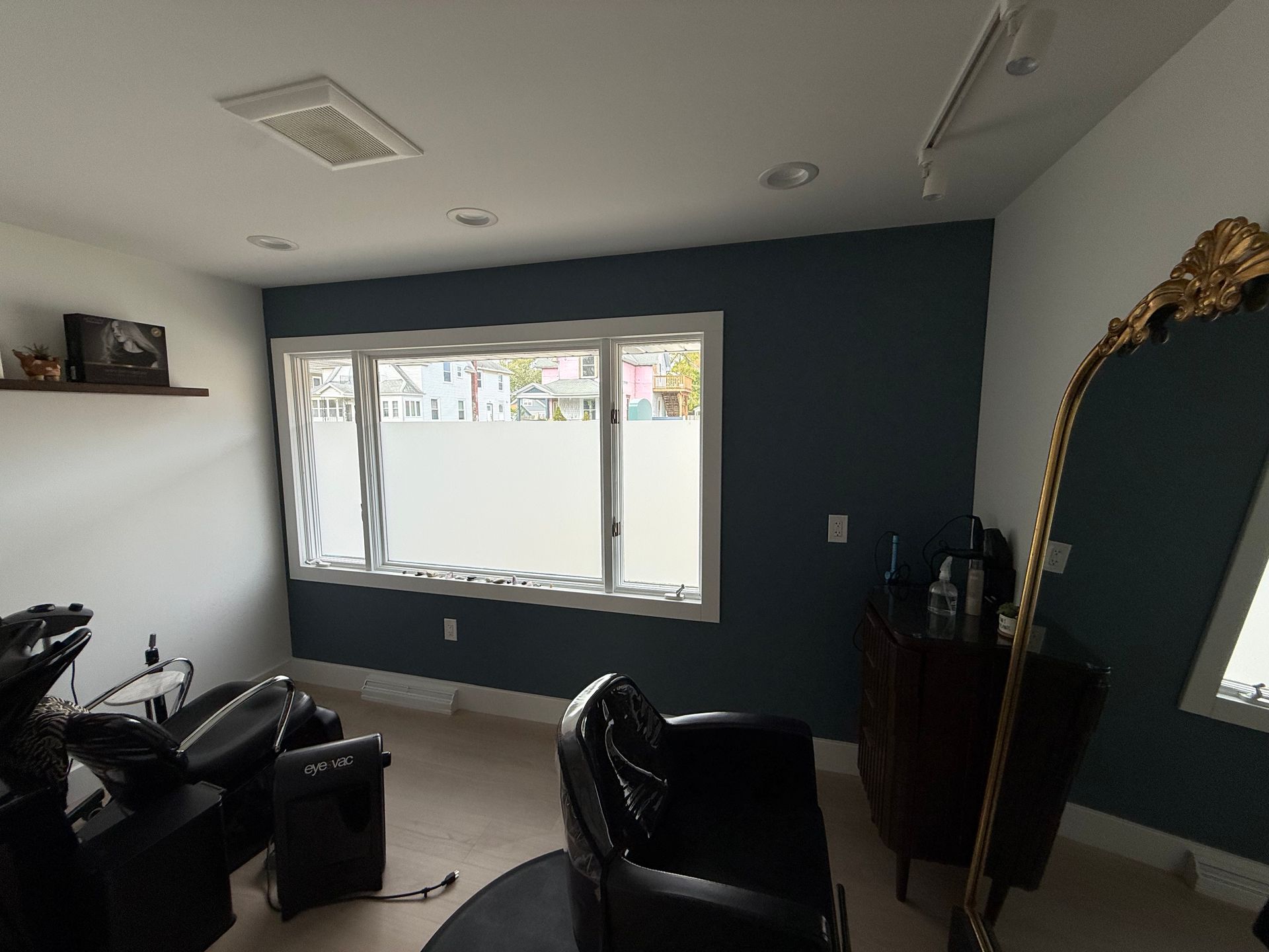 Modern living room with dark teal accent wall, large window, black chairs, and ornate gold-framed mirror