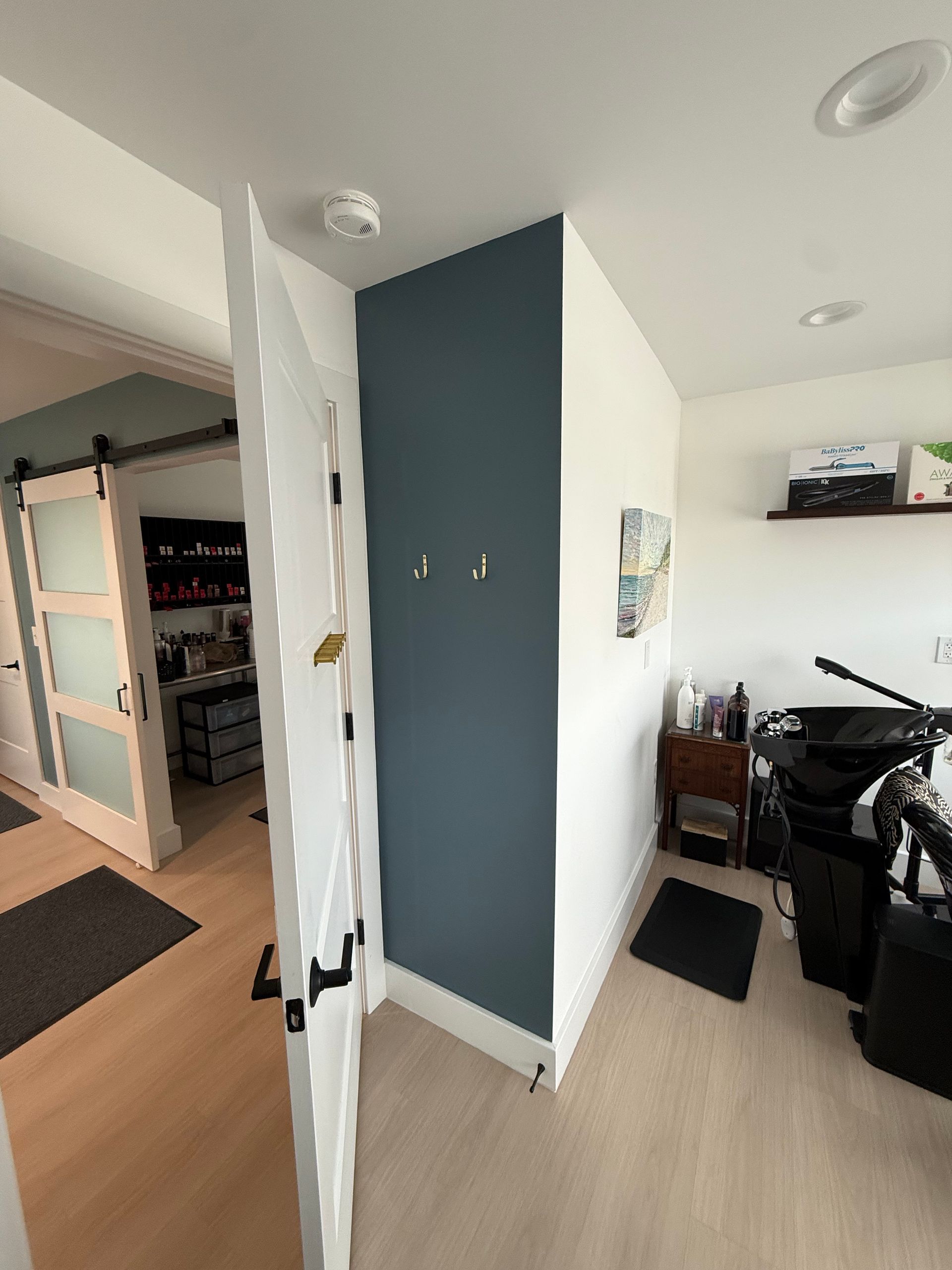 Bright hallway with open door, teal accent wall, and a room with exercise equipment and storage crates.
