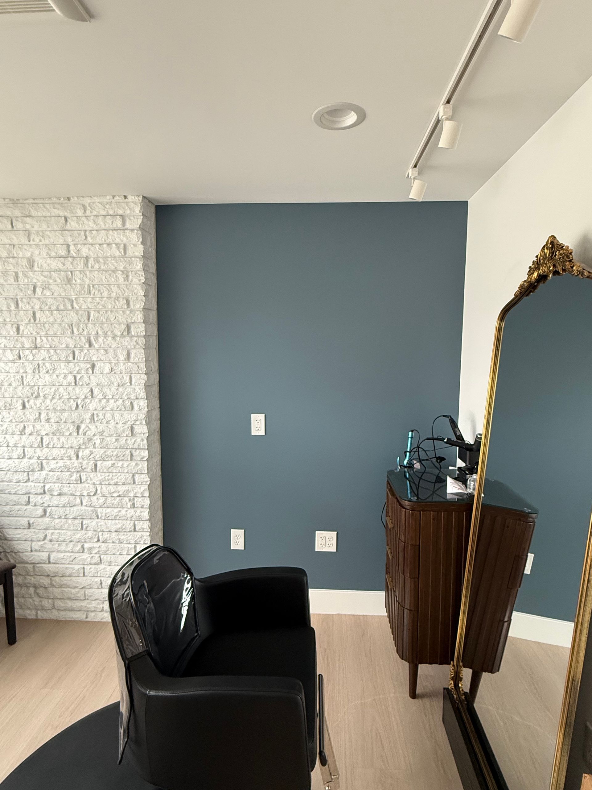 Modern room with blue accent wall, white brick wall, black chair, and ornate mirror.