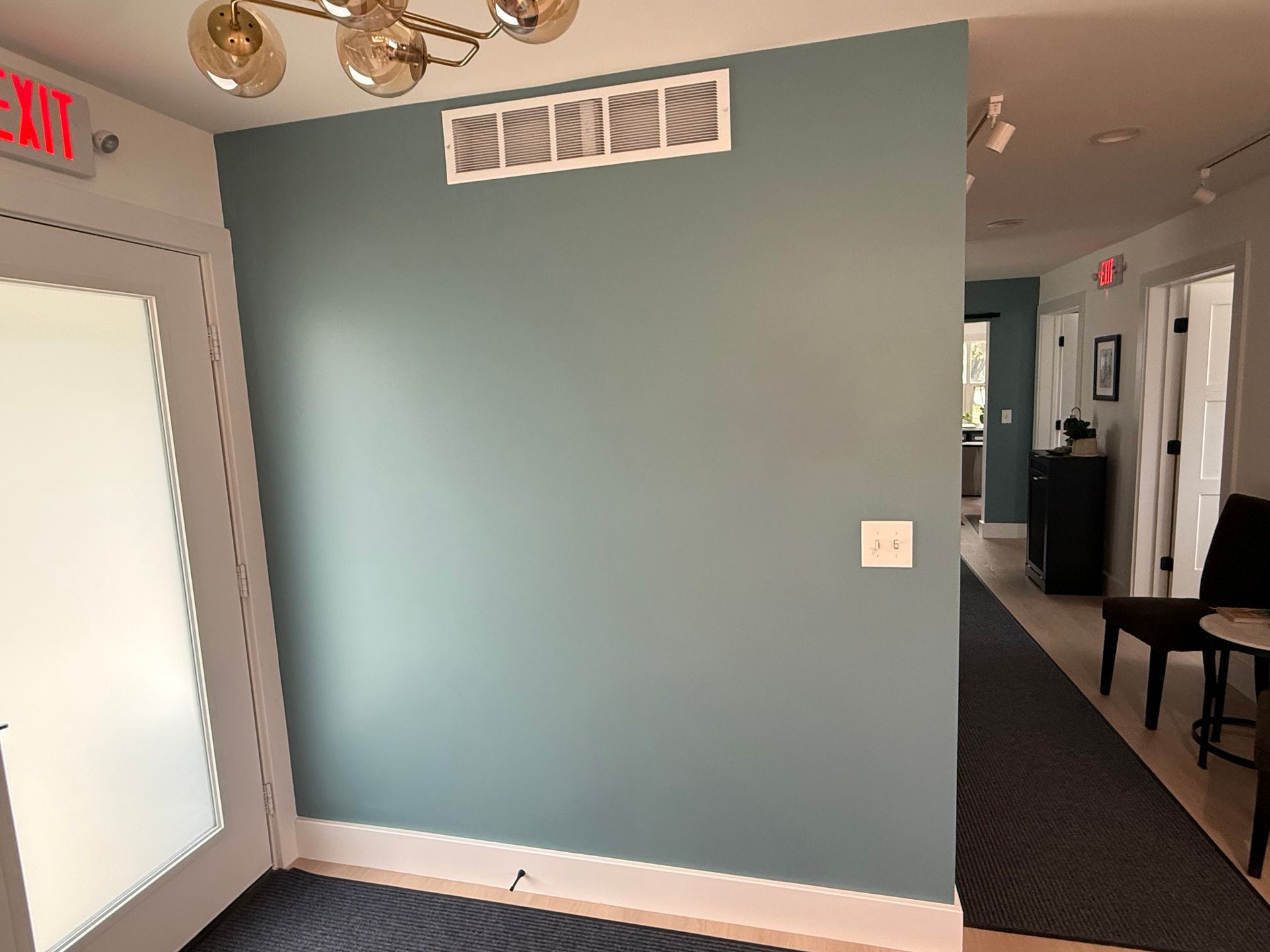 Empty hallway with teal accent wall, frosted door, and carpeted corridor extending into the distance.