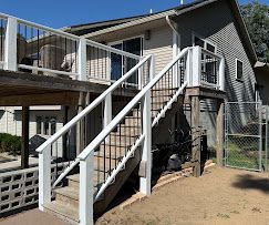 White outdoor stairs leading to a raised house deck, beside a gray home with a chain-link fence