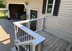 Front porch with white railing, wooden steps, and driveway view beside a beige house