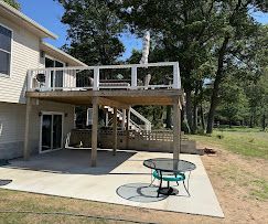Backyard deck with staircase, white railing, and round patio table on a concrete patio.