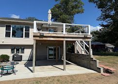 Back deck and patio with stairs, white railing, and concrete slab behind a house
