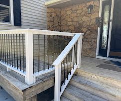 Front porch with stone wall, white railing, and steps leading to a dark front door.