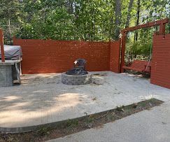Backyard patio with a circular fire pit, red fence, and trees in the background