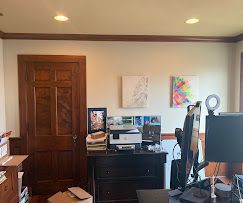 Home office with desk, computer monitors, printer, and wooden door in a softly lit room