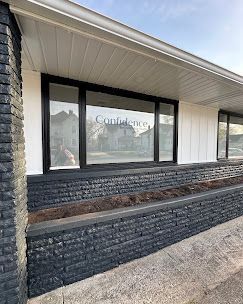 Building exterior with dark stone facade, large window, and white siding under a sloped roof