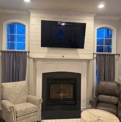 Living room fireplace with wall-mounted TV, flanked by two windows and two upholstered chairs
