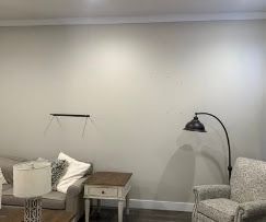 Empty living room wall with a side table, chairs, and a black floor lamp casting shadows
