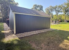 Gray backyard shed with a sloped roof, sitting on gravel beside a grassy yard and trees.