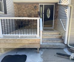 Front porch with steps, railing, stone wall, and black front door with oval glass panel