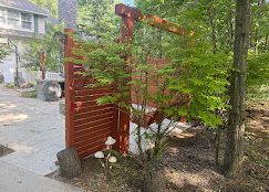 Red wooden privacy screen with a young tree beside a house and driveway