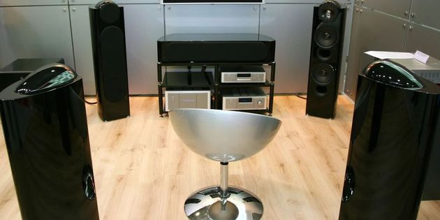Modern living room with black speakers, TV stand, and a silver swivel chair on a light wood floor