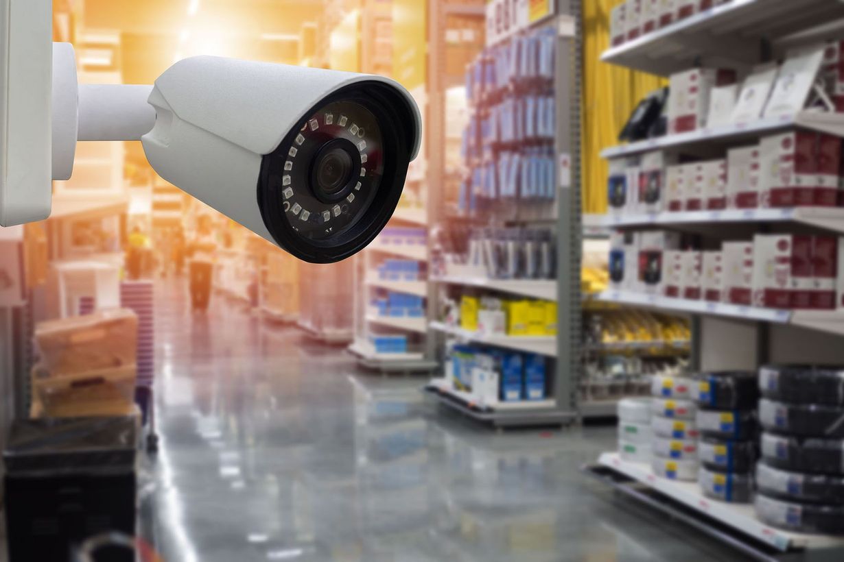 Security camera mounted in a brightly lit store aisle with shelves in the background