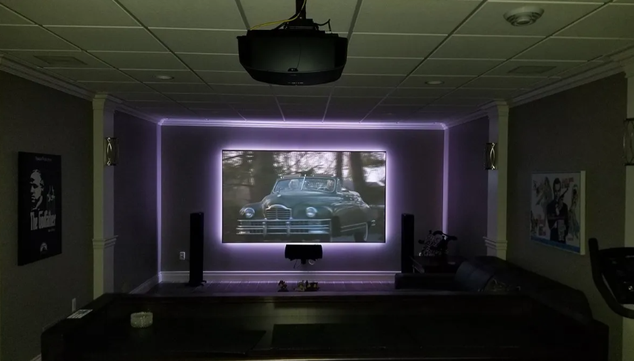 Dim home theater with a glowing purple screen frame and a movie playing on the projector screen
