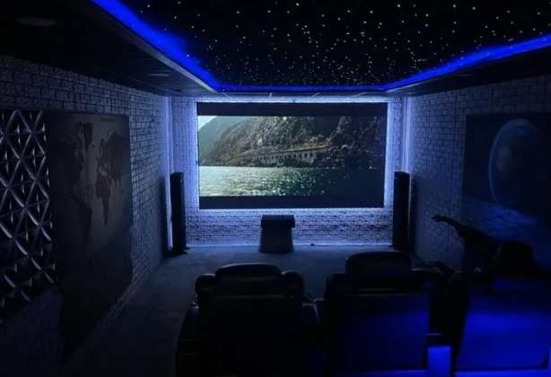 Dark home theater with blue LED lighting, facing a large screen showing a lake and cliffs