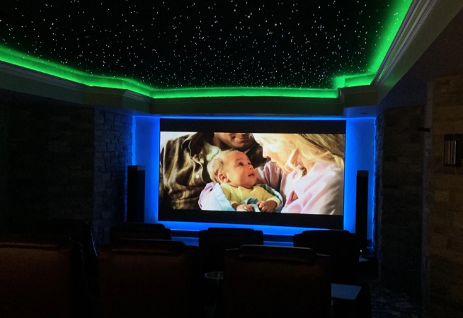 Dim home theater with green ceiling lights and a TV showing a parent holding a baby