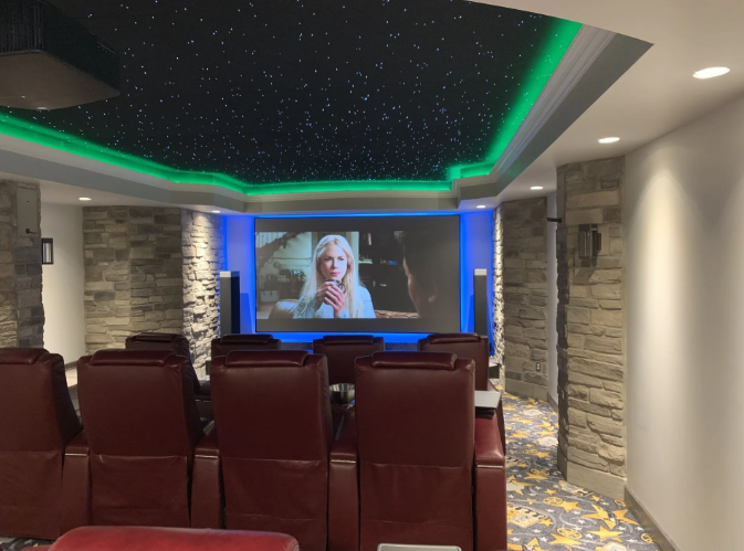 Home theater with red seats, a ceiling starfield, and a movie playing on the screen.