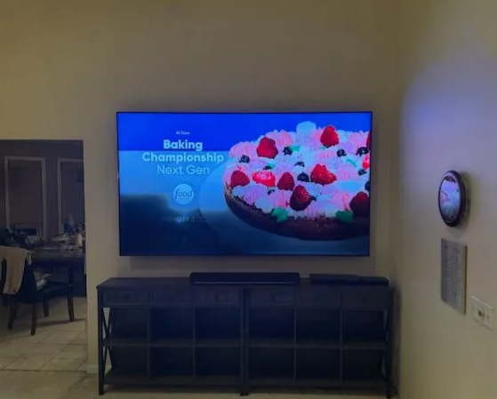 Living room with wall-mounted TV showing a baking challenge and a cake, above a dark media console
