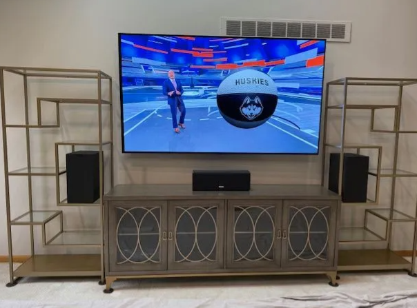 Living room with TV on a media console, flanked by decorative shelves and speakers