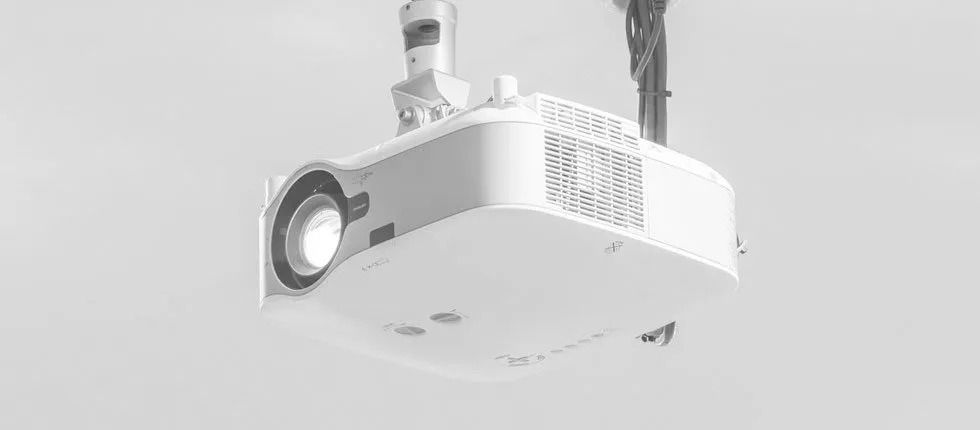 White ceiling-mounted projector angled downward, showing its lens and vents