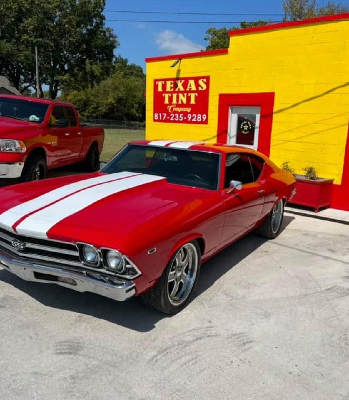 Red classic car with white stripes parked in front of a yellow building labeled 