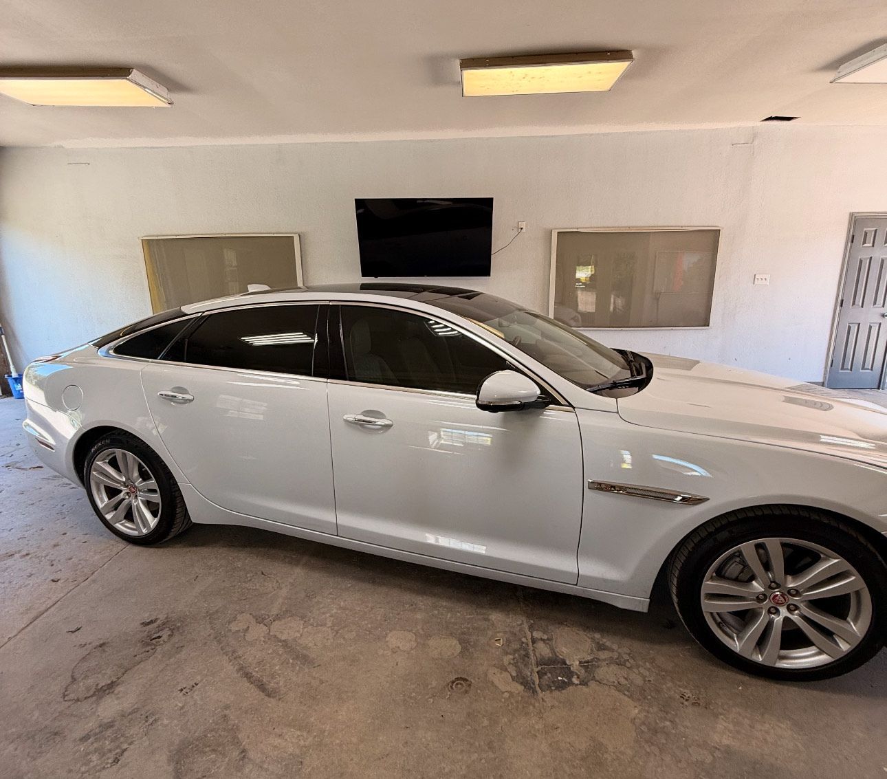 White Jaguar sedan parked inside a garage, next to what seems to be a TV.
