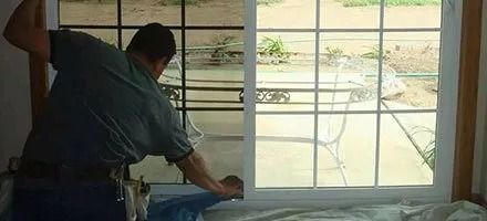 A person installing a window with a patio view.