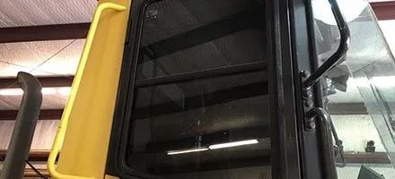 Yellow construction equipment cab with a black framed window.