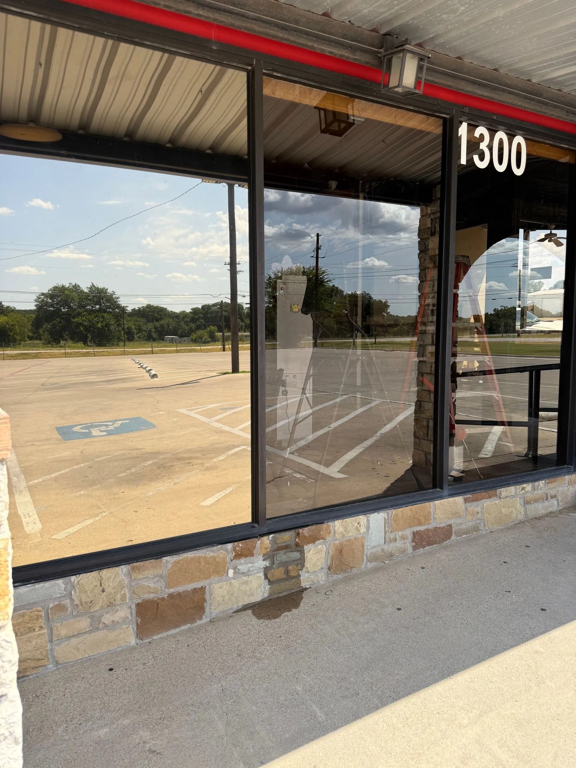 Storefront with large windows reflecting a parking lot and sky. Building has stone and brick exterior.
